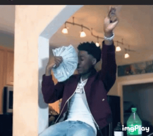 A Man In A Maroon Jacket Is Holding A Fan Of Money In His Hands . GIF