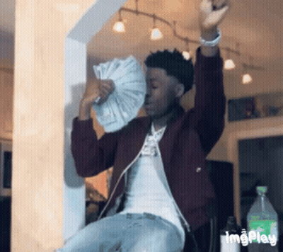 A Man In A Maroon Jacket Is Holding A Fan Of Money In His Hands . GIF