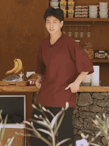 A Man In A Maroon Shirt Is Standing In Front Of A Shelf With Bowls On It GIF