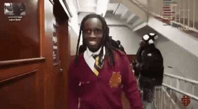 A Man In A Maroon Sweater And Tie Is Walking Down Stairs GIF