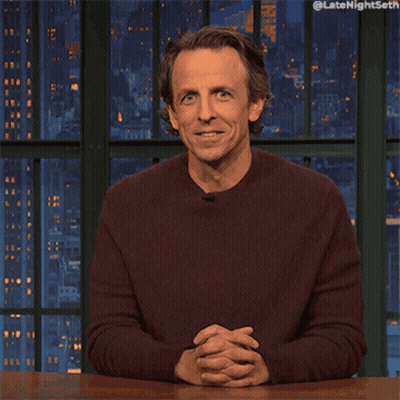 A Man In A Maroon Sweater Is Sitting At A Table With His Hand On His Chin And The Words Late Night Seth On The Bottom GIF