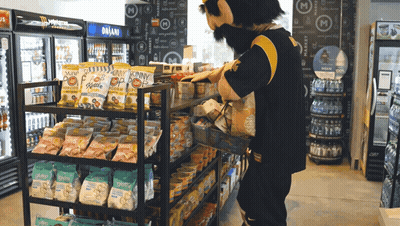 A Man In A Mascot Costume Is Standing In Front Of A Display Of Snacks GIF