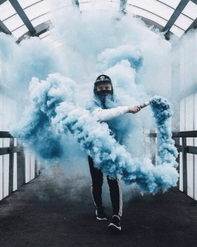 A Man In A Mask Holds A Blue Smoke Bomb In His Hand GIF