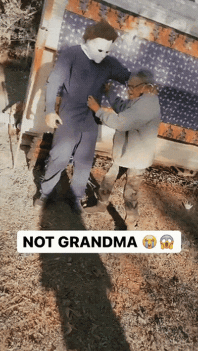 A Man In A Mask Is Being Helped By An Elderly Woman With The Words Not Grandma Below Him GIF
