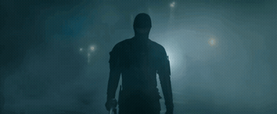 A Man In A Mask Is Holding A Gun In A Dark Room . GIF