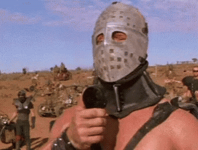 A Man In A Mask Is Holding A Microphone In A Desert . GIF