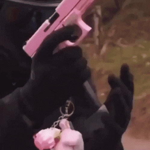 A Man In A Mask Is Holding A Pink Gun In His Hands . GIF