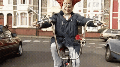 A Man In A Mask Is Riding A Bicycle Down A Street . GIF