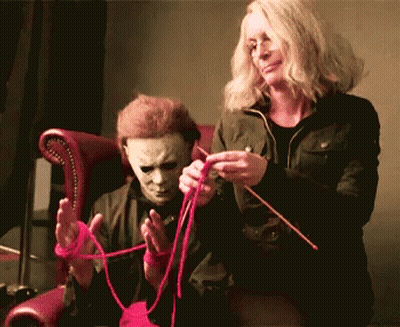 A Man In A Mask Is Sitting Next To A Woman Who Is Knitting GIF