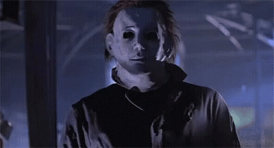 A Man In A Mask Is Standing In A Dark Room And Looking At The Camera . GIF