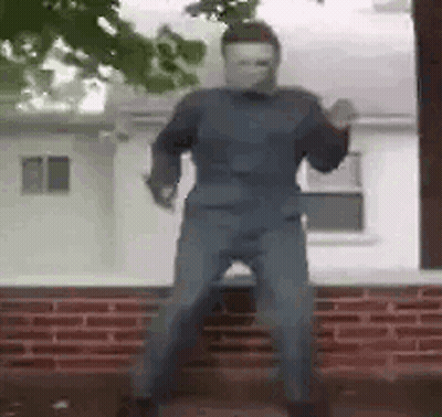 A Man In A Mask Is Standing In Front Of A Brick Building . GIF