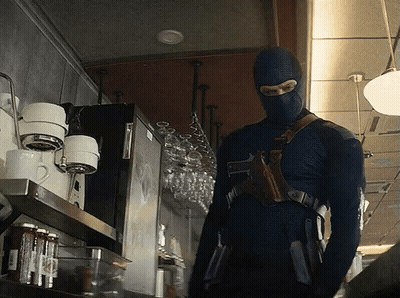 A Man In A Mask Is Standing In Front Of A Coffee Machine GIF