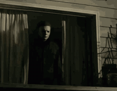 A Man In A Mask Is Standing In Front Of A Window In A Dark Room . GIF