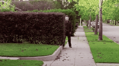 A Man In A Mask Is Walking Down The Sidewalk GIF