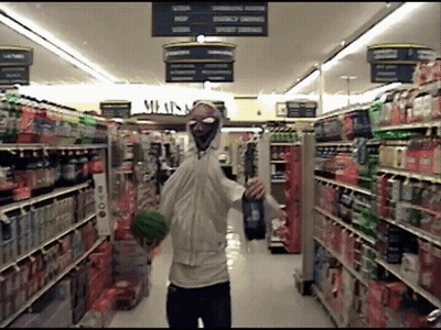 A Man In A Mask Is Walking Through A Grocery Store Aisle With A Sign That Says Meats GIF