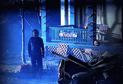 A Man In A Mask Stands In Front Of A House With Pumpkins On It GIF