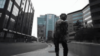 A Man In A Mask Walks Down A Street In Front Of A Building GIF