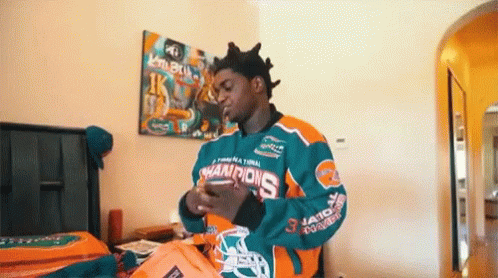 A Man In A Miami Dolphins Jersey Is Standing In A Bedroom Holding A Bag . GIF