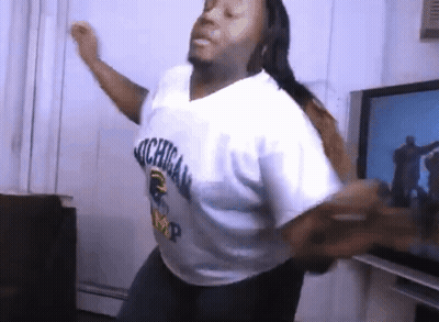 A Man In A Michigan Shirt Is Dancing In A Living Room GIF