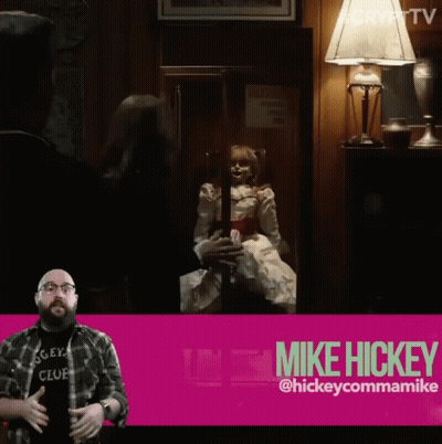 A Man In A Mickey Club Shirt Stands In Front Of A Pink Sign That Says Mike Hickey GIF