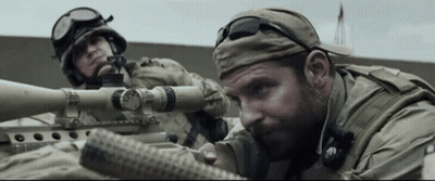 A Man In A Military Uniform Is Aiming A Sniper Rifle . GIF