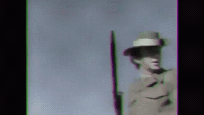 A Man In A Military Uniform Is Holding A Rifle Against A Blue Sky . GIF