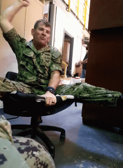 A Man In A Military Uniform Is Sitting In A Chair With His Arms In The Air GIF