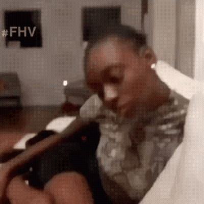 A Man In A Military Uniform Is Sitting On A Couch In A Living Room Holding A Book . GIF
