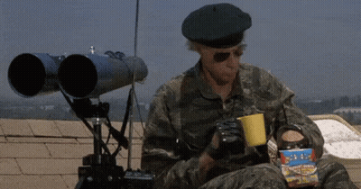 A Man In A Military Uniform Is Sitting On A Roof Holding A Cup Of Coffee And A Box Of Popcorn . GIF