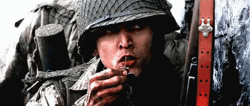 A Man In A Military Uniform Is Smoking A Cigarette With A Cross In His Mouth GIF