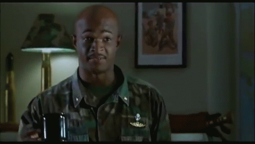 A Man In A Military Uniform Is Standing In A Room With A Lamp And A Picture On The Wall . GIF