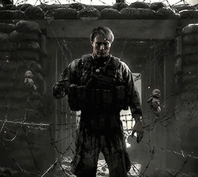 A Man In A Military Uniform Is Standing In Front Of A Barbed Wire Fence Holding A Baby . GIF