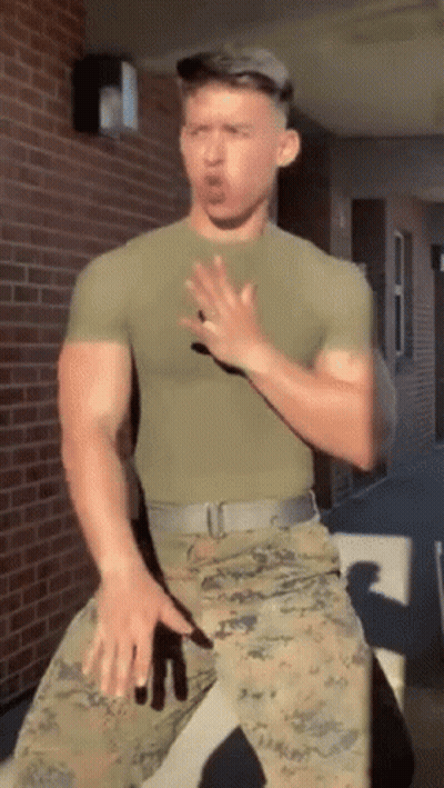 A Man In A Military Uniform Is Standing In Front Of A Brick Building Making A Funny Face . GIF