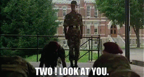 A Man In A Military Uniform Is Standing In Front Of A Brick Building While Two Other Soldiers Look At Him . GIF