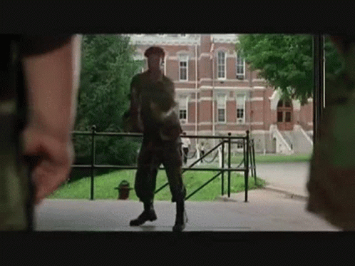 A Man In A Military Uniform Is Standing In Front Of A Building . GIF