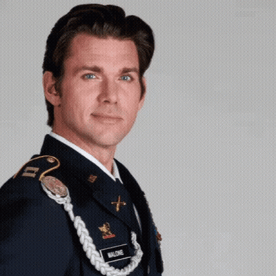 A Man In A Military Uniform Is Standing In Front Of A Sign That Says Superhero GIF