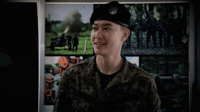 A Man In A Military Uniform Is Standing In Front Of A Wall With Pictures Of Soldiers On It GIF