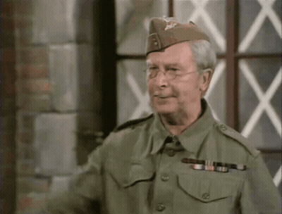 A Man In A Military Uniform Is Standing In Front Of A Window And Smiling GIF