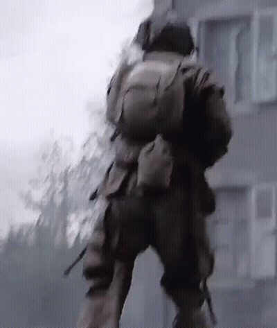 A Man In A Military Uniform Is Walking In Front Of A Building With A Backpack On His Back . GIF