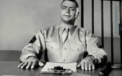 A Man In A Military Uniform Sits At A Desk In Front Of A Prison Cell GIF