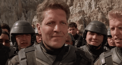 A Man In A Military Uniform Stands In A Crowd Of People GIF