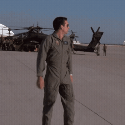 A Man In A Military Uniform Stands On A Runway In Front Of A Black Helicopter GIF