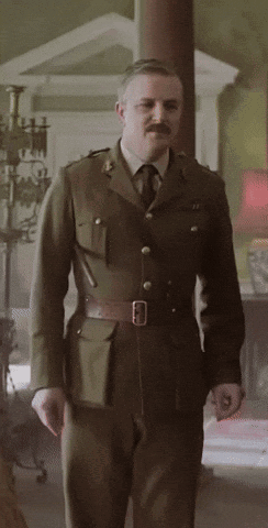 A Man In A Military Uniform With A Mustache Is Standing In A Room GIF