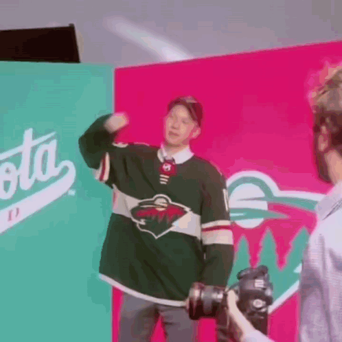 A Man In A Minnesota Wild Jersey Is Being Photographed By A Cameraman . GIF