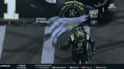 A Man In A Monster Shirt Stands In Front Of A Car That Says Good Year GIF