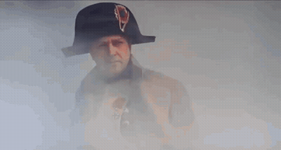 A Man In A Napoleon Hat And Coat Is Standing In Front Of A Building . GIF