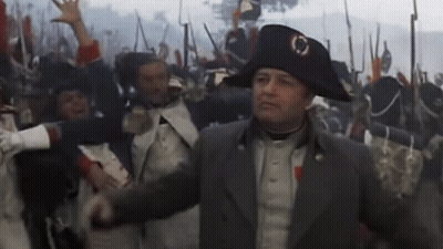 A Man In A Napoleon Hat Stands In Front Of A Crowd GIF