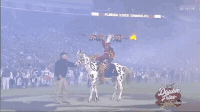 A Man In A Native American Costume Stands On A Football Field With A Horse GIF