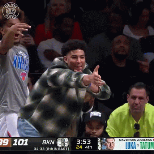 A Man In A New York Knicks Shirt Is Giving A Thumbs Up During A Basketball Game GIF