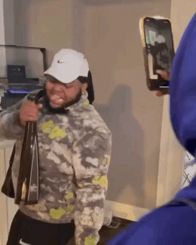A Man In A Nike Hat Is Holding A Bag And Taking A Picture Of Himself With A Phone . GIF